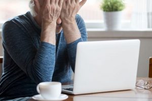 Senior Man Sitting at a Computer and Covering his Eyes with his Hands